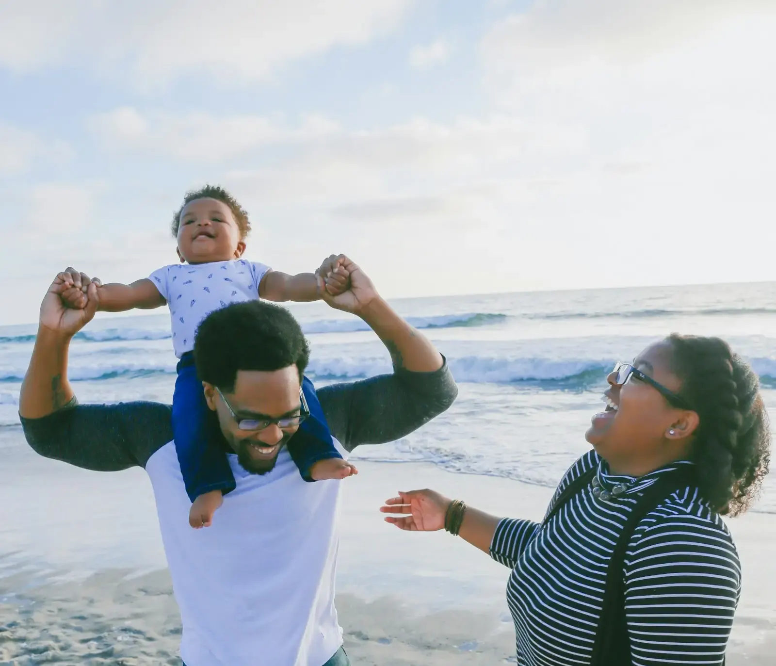 A caregiver carries a young child along the beach