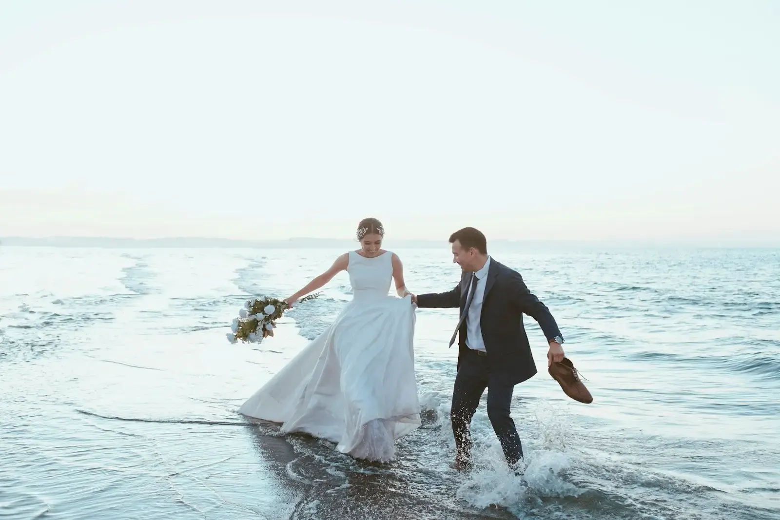 A newly married couple holds hands on the shoreline