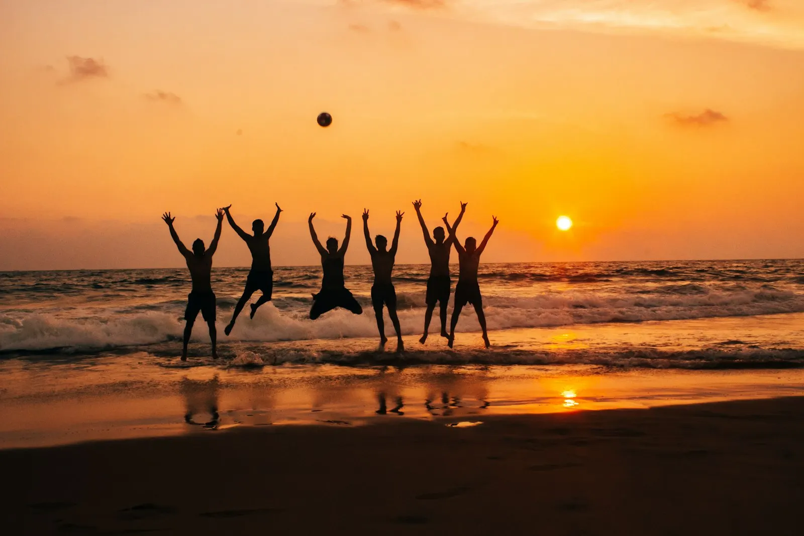 A group of friends jumping together on the beach at golden hour