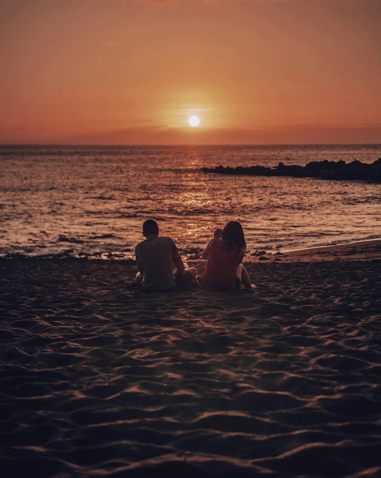 A man and woman sitting together on an Aruba beach during golden hour