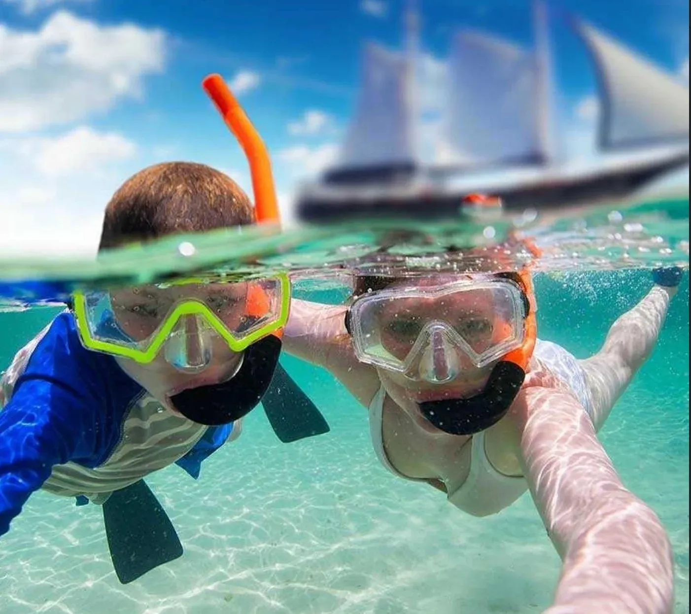 A parent and child snorkeling together with the Flagship Aruba schooner visible in the background